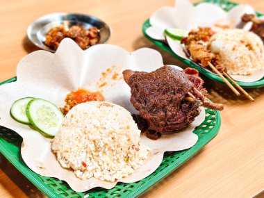 Baharatlı pirinç, acı biber sosu ve dilimlenmiş salatalık ile servis edilen Madura usulü siyah baharatlı ördek, yağsız kağıtla kaplı plastik bir sepet üzerinde servis edilir. Bir gurme Endonezya yemeği.