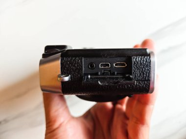 Bir adam eli üzerinde sentetik deri bir vücut ve ses deliği ve USB HDMI portu için bir örtü ile gümüş boyanmış aynasız kameranın yan yüzünü gösteriyor.