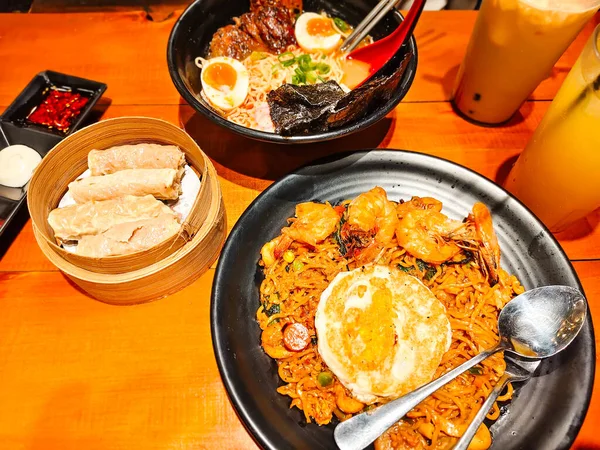 A hearty bowl of delicious fried seafood ramen noodles and beef ramen in tori paitan soup with a side dish of shrimp dim sum on a bamboo tray. Asian cuisine at a restaurant