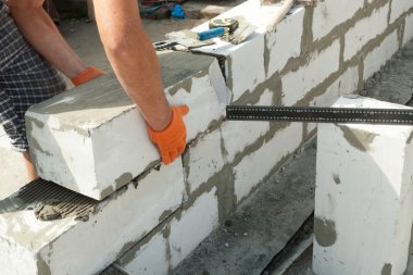 Mason, inşa edilmiş ev duvarının havalandırmalı beton bloğunu hizalıyor.