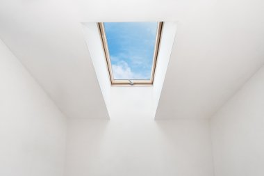A modern open skylight (mansard window) in an attic room against blue sky clipart
