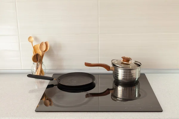 Öppna kastrull, stekpanna och träskedar i modernt kök med induktionsspis — Stockfoto