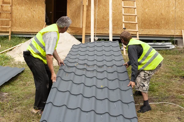 Two workers preparing to install a metal tile on a new wooden house — Stock Photo, Image