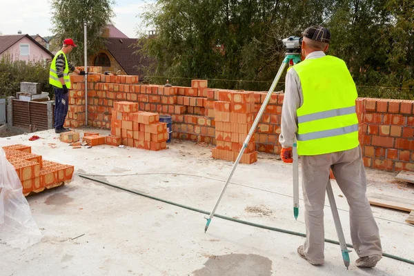 En arbetstagare med teodolit kontrollerar giltigheten av bricklayingen — Stockfoto