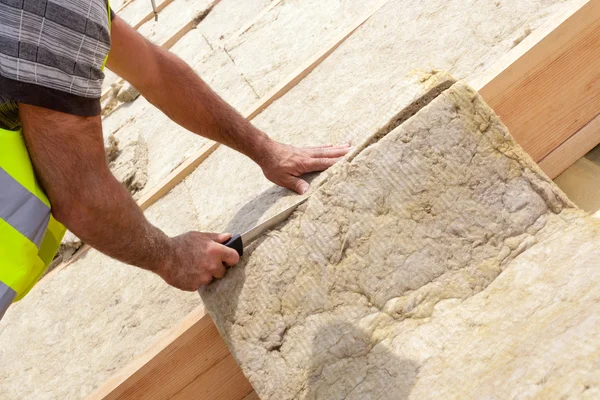 Roofer builder worker installing roof insulation material on new house under construction. Cutting rockwall with sharp knife — Stock Photo, Image
