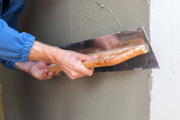 Construction worker with long trowel plastering a wall