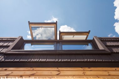 Kiremit mavi gökyüzü karşı olan ahşap evde açık tepe (mansard windows)