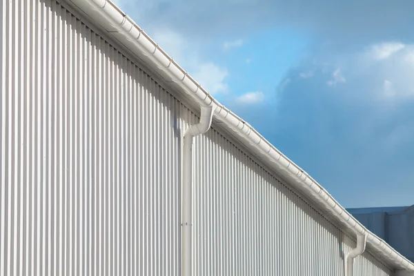 Nova calha de chuva branca em um prédio com folha de metal branco contra o céu azul — Fotografia de Stock