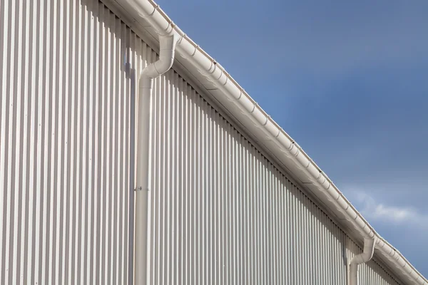 Nieuwe witte regengoot op een gebouw met wit metaal blad tegen blauwe hemel — Stockfoto