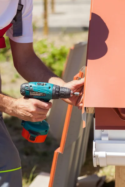 Worker on a roof with electric drill installing red metal tile on wooden house — Stock Photo, Image