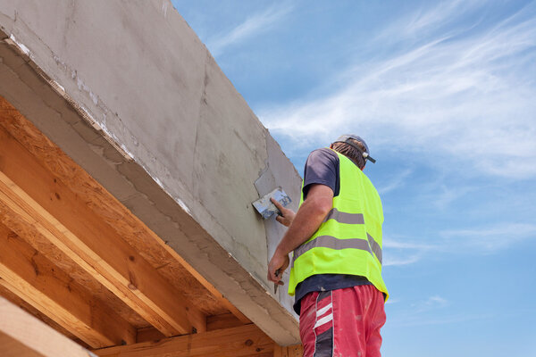 Construction worker with trowel plastering a facade of a new house