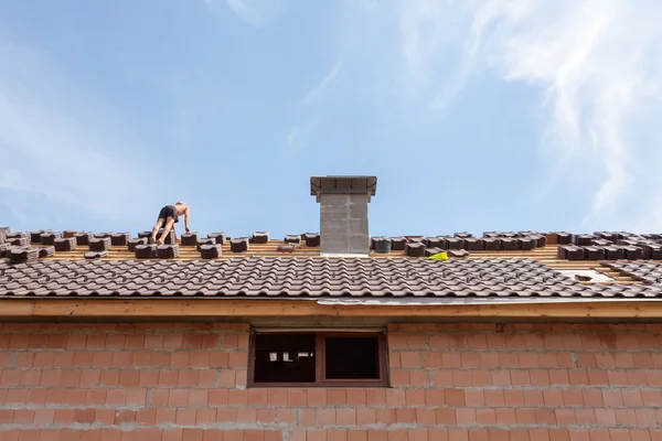 Techos: trabajador de la construcción en un techo que lo cubre con azulejos - renovación del techo: instalación de papel de alquitrán, azulejos nuevos y chimenea —  Fotos de Stock