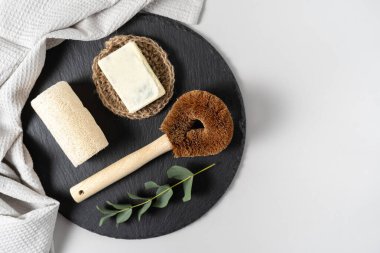 Mutfak malzemelerinde sıfır atık kavramı. Düz yerde, mutfak hindistan cevizi fırçası, luffa süngeri, katı sabun, havlu ve okaliptüs bitkisi beyaz fotokopi alanı arka planına karşı siyah plaka standı üzerinde.