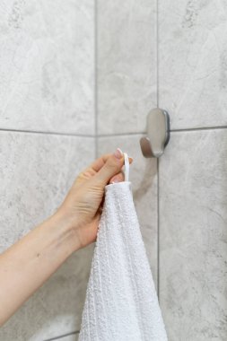 Dikey kesilmiş kadın eli görüntüsü modern banyodaki kancaya asılı beyaz banyo havlusu ile kaplanmış fotokopi duvarı