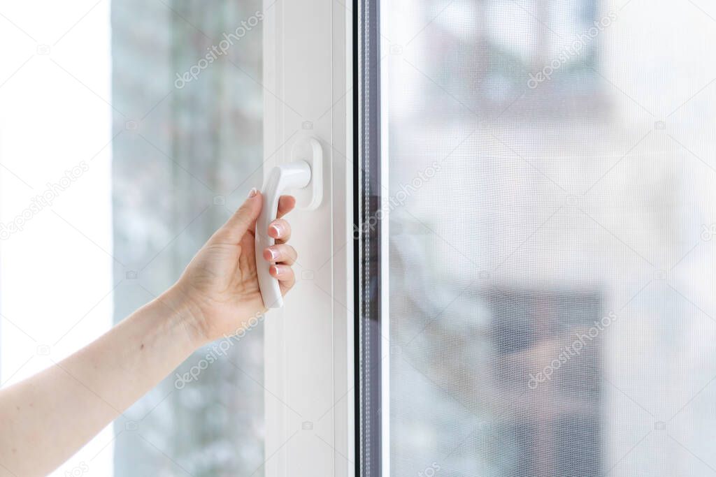 Cropped view of woman closing plastic window in her house. Selective focus of housewife hand holding handle at pvc frame with double glazing