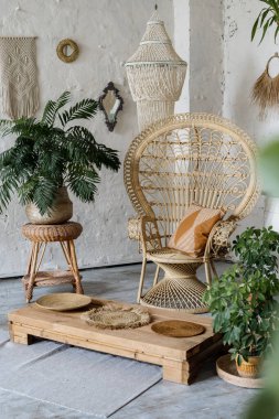 Hasır koltuk, döşeme masası, dekor, konforlu oturma odasında yeşil ev bitkileri ve iç dizaynı bohem tarzında. Güzel ve rahat yatak odasının bir parçası