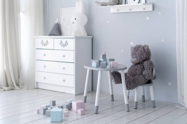 Oyuncak ayı, beyaz klozet, oyuncak ve dekorlu çocuk oyun odasında tahta küplerle masanın arkasında oturuyor. Minimalist iç mimari tarzlı bir yatak odası.