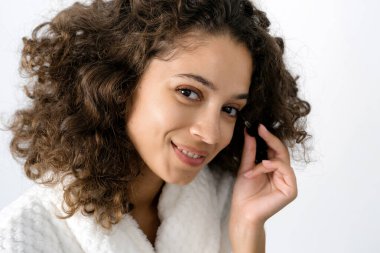 Cilt bakımı konsepti. Yüzünde kırışıklık önleyici serumu olan bornozlu, gülümseyen Afro-Amerikan kadını yakından çek. Sabahları banyoda kameraya bakarak geçir.