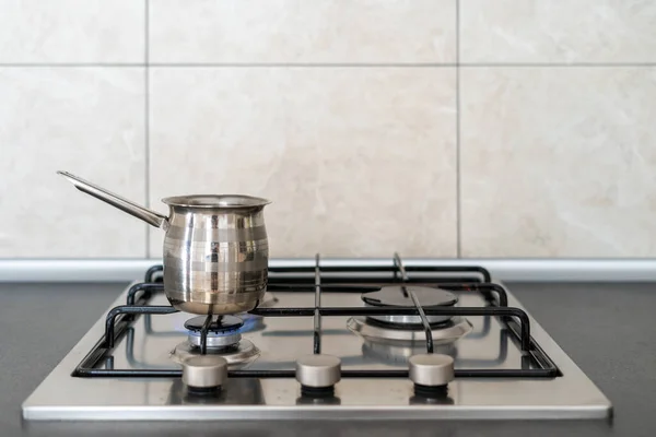 Small stewpan with beverage standing on modern kitchen gas stove cooker with fired metal burner against copy space background