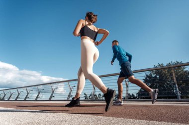 Egzersiz ve egzersiz kavramı. Motive olmuş yetişkin sporcu kadın ve erkeğin açık havada spor eğitimi alıp şehirde hızlı koşmalarının düşük açılı görüntüsü.