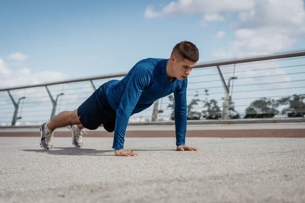 Morning exercise and workout concept. Low angle view of adult strong and focused sportsman making sport training outdoors alone, doing push ups exercise and standing in plank pose