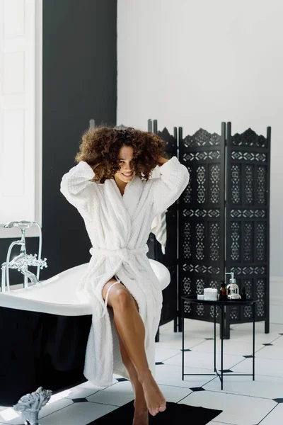 早上淋浴和日常活动的概念 纵观身穿浴衣的快乐笑容满面的年轻非洲裔美国女人看着相机 在浴室里呆着 — 图库照片
