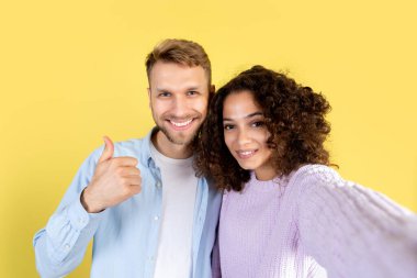 Video görüşmesi ve sosyal mesafe kavramı. Adam afro-amerikan kadınını kamerada kendi portresini çekerken kucaklıyor. Sarı arkaplanda fotokopi alanı ile birlikte duran insanlar