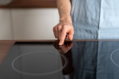 Elektrikli ocağın güç düğmesinde cam seramik yüzeyi olan bir kadın vardı. Bulanık kopya alanı arka planına karşı modern mutfakta duran ev hanımı