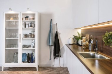 İç tasarım, beyaz mutfak dolapları, dolapta mutfak malzemeleri, ahşap tezgahta boş ve temiz lavabo, kancada önlük.