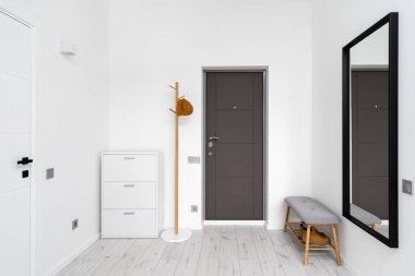 Modern iç tasarımı modern dairede olan minimalist koridor. Beyaz duvardaki siyah çerçeve aynasının yanında rahat bir ayakkabı deposu. Salonda göğüs çekmeceleri olan ahşap bir elbise askısı.