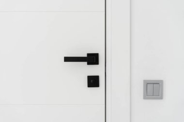 Modern minimalist kapının yanındaki beyaz duvardaki siyah saplı ışık düğmesini kapat. Çağdaş iç tasarım ayrıntıları evde, dairede veya ofiste