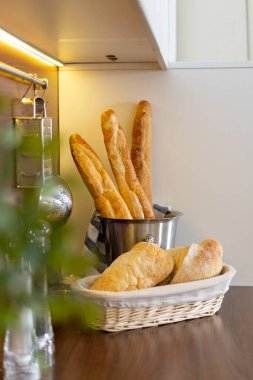 Mutfaktaki ahşap tezgahın üzerinde ev yapımı taze ekmek ve Fransız ekmeği olan sepetin dikey görüntüsü. Konforlu ev konseptinde çağdaş iç mekan