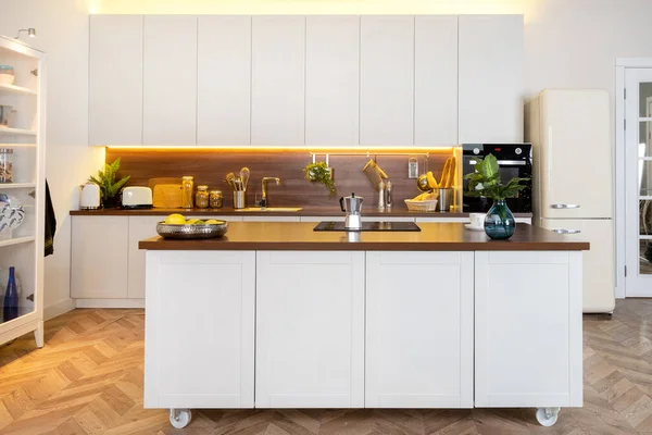 Domestic life and household equipment concept. Front view of contemporary interior with white kitchen cupboards, wooden countertop, geyser coffee maker on ceramic glass stove against electric oven