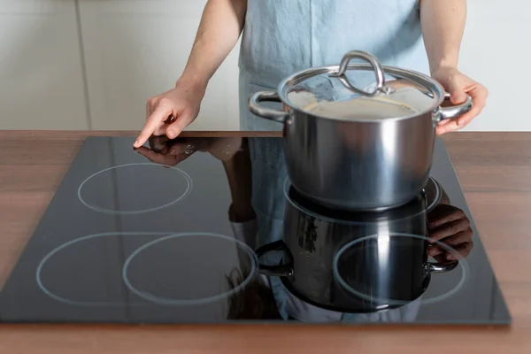 妇女站在现代化厨房里 用平底锅烹调食物 用手指按电炉玻璃陶瓷表面的电钮的剪影 — 图库照片