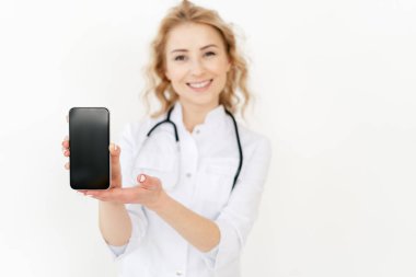 Online danışmanlık, tıbbi asistan uygulaması. Beyaz önlüklü doktor, steteskopla ayakta duruyor, dokunmatik ekranlı akıllı telefonu fotokopi cihazıyla gösteriyor. Sağlık teknolojisi ve sağlık sigortası kavramı