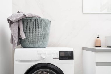 Ev işi konsepti. Çamaşır sepetinin içinde havlular ve giysiler vardı. Parlak banyo içindeki otomatik çamaşır makinesinin üzerinde duruyordu.