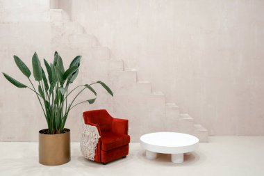 Kırmızı koltuk, beyaz kahve masası ve çiçek saksısında fotokopi arkaplanındaki merdivenlerin önünde duran saksı. Mobilya tasarımı ve modern iç mimari kavramı