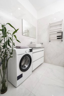 Yeni otomatik çamaşır makinesi, seramik lavabo, beyaz dolaplar, ayna ve ısıtılmış havlu tırabzanı olan daireye dikey bakış modern iç tasarımla birlikte banyoda fayanslı duvarda.