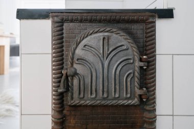 Evdeki camlı beyaz fayanslardan yapılmış odun yakan pişirme sobasının üzerinde eski moda dökme demir şömine kapısının yakın çekimi. Ev ısıtma ve geleneksel mutfak aletleri konsepti