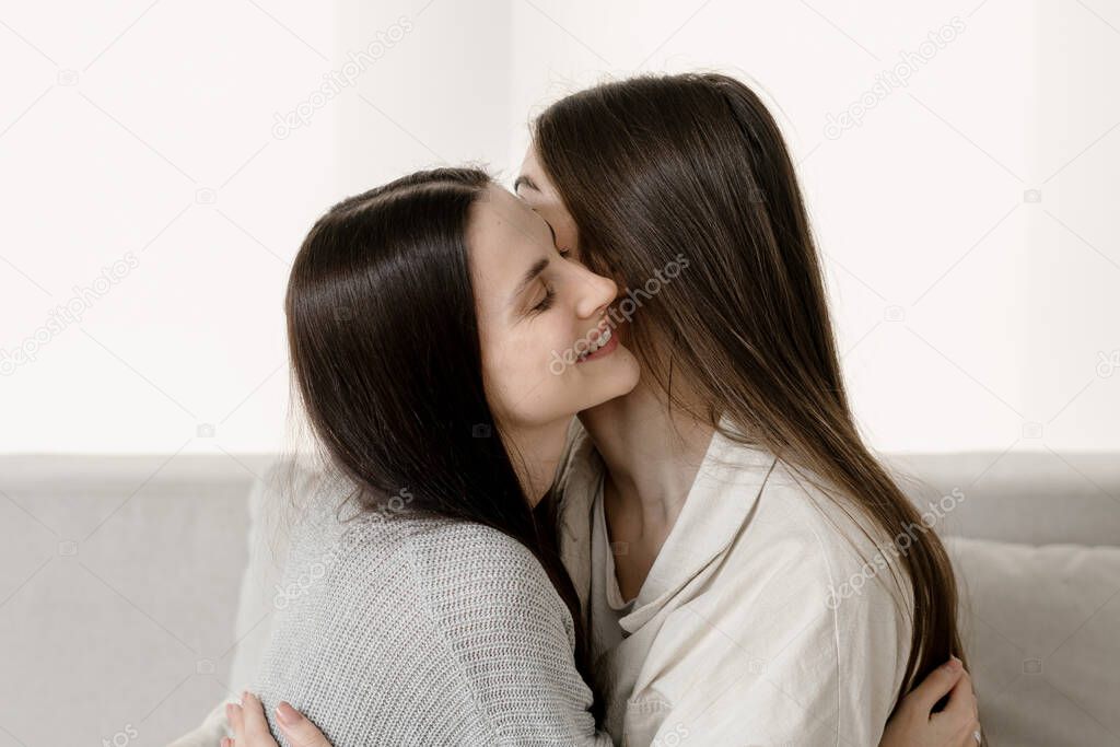 Concept of tender moment in friendship. Two happy girls best friends glad to see each other after long separation. Women embracing and smiling wide, standing indoors