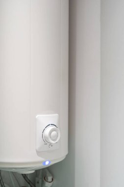 Duvarında kontrol düğmesi ve ışık göstergesi asılı beyaz banyo kazanının dikey görüntüsü. Modern evde su ısıtma.