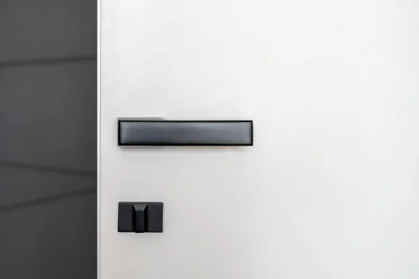 黒いマットのドアハンドルと安全ロックが自宅やホテルの部屋でミニマリストスタイルで行われた白いドアのクロップショット — ストック写真