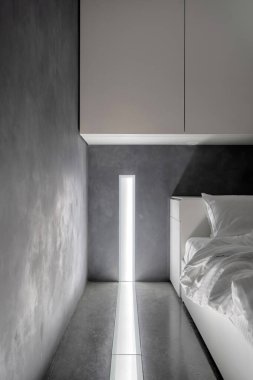 Modern otel odasındaki rahat yatağın üzerinde asılı beyaz dolapların dikey görüntüsü. Modern apartmanda ışık sistemi ve gece lambası var.