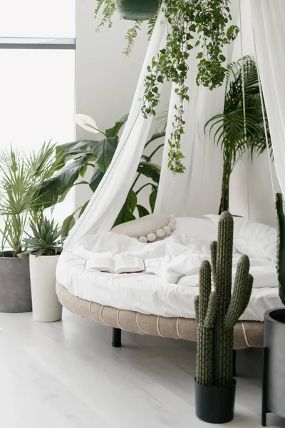 Modern cozy bedroom with round canopy bed and green tropical plants, vertical shot. Contemporary apartment with bohemian interior style. Lazy morning at home and perfect place for relaxation concept