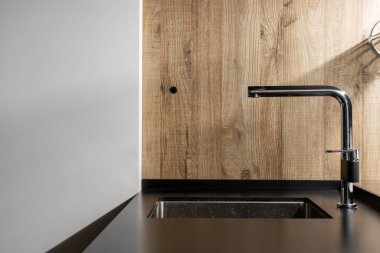 Mat tezgahlı krom musluk ve siyah renkli lavabo, minimalist iç mekanda ahşap desenli yapı olan duvarın karşısında şık bir mutfak.
