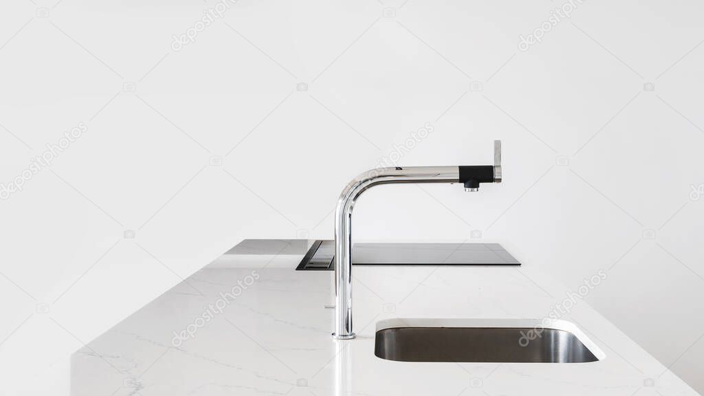 White clean kitchen counter with modern shiny faucet and square metal sink with built-in glass stove top, with nobody in sight on light background with minimalist setting, copy space for text