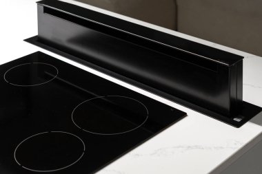 State of black ceramic induction stove top with retractive exhaust device on clean countertop with white surface, convenient modern kitchen technology with nobody in picture, close up clipart