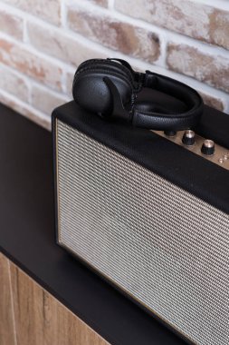 Dikey çekim siyah kablosuz kulaklıklar modern ses sütunu üzerine uzanan koyu kahverengi masa üzerinde tuğla duvar arka plan iç. Müzik ekipmanları konsepti
