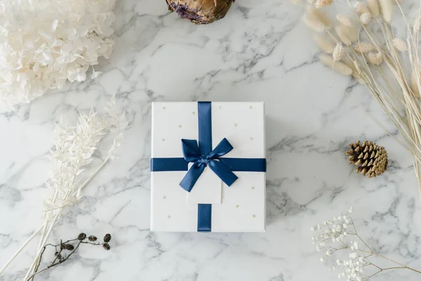 White box with blue bow and ribbon on table with decorative marble surface, gift with label for someone special, celebrating something important. Holidays and celebration concept