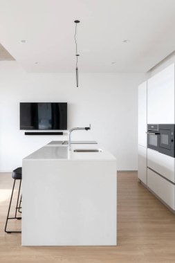 Modern mutfak tasarımı hafif temalı, beyaz tezgah, siyah tabure, musluk, lavabo ve cam soba, fırın ve mikrodalga fırın ile yapılmış büyük dolap. Dikey çekim